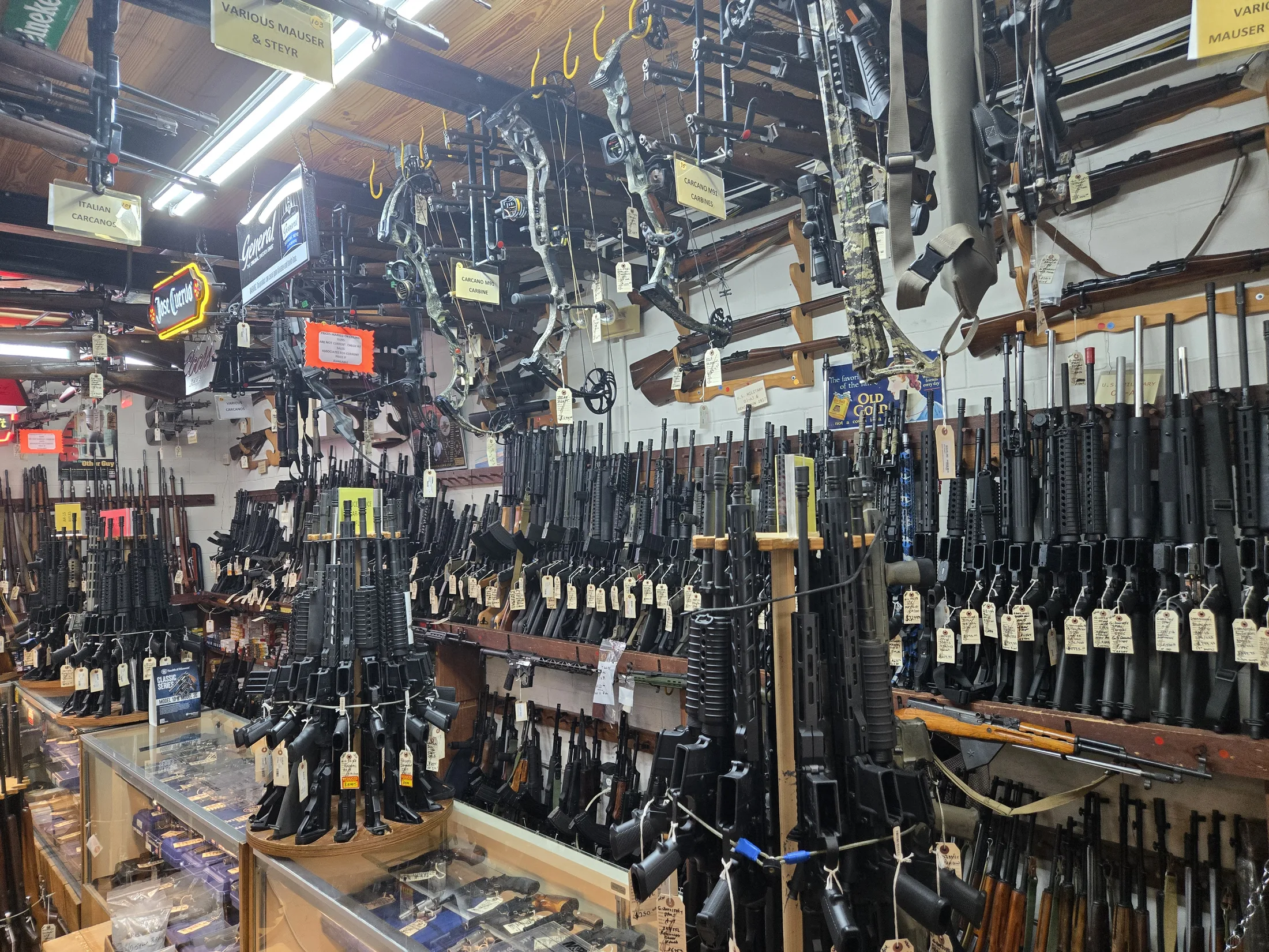 Rifle racks at AAA Gun & Pawn with compound bows displayed above